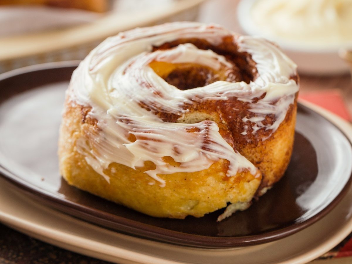 Rollo de canela con glaseado de queso crema servido en un plato oscuro