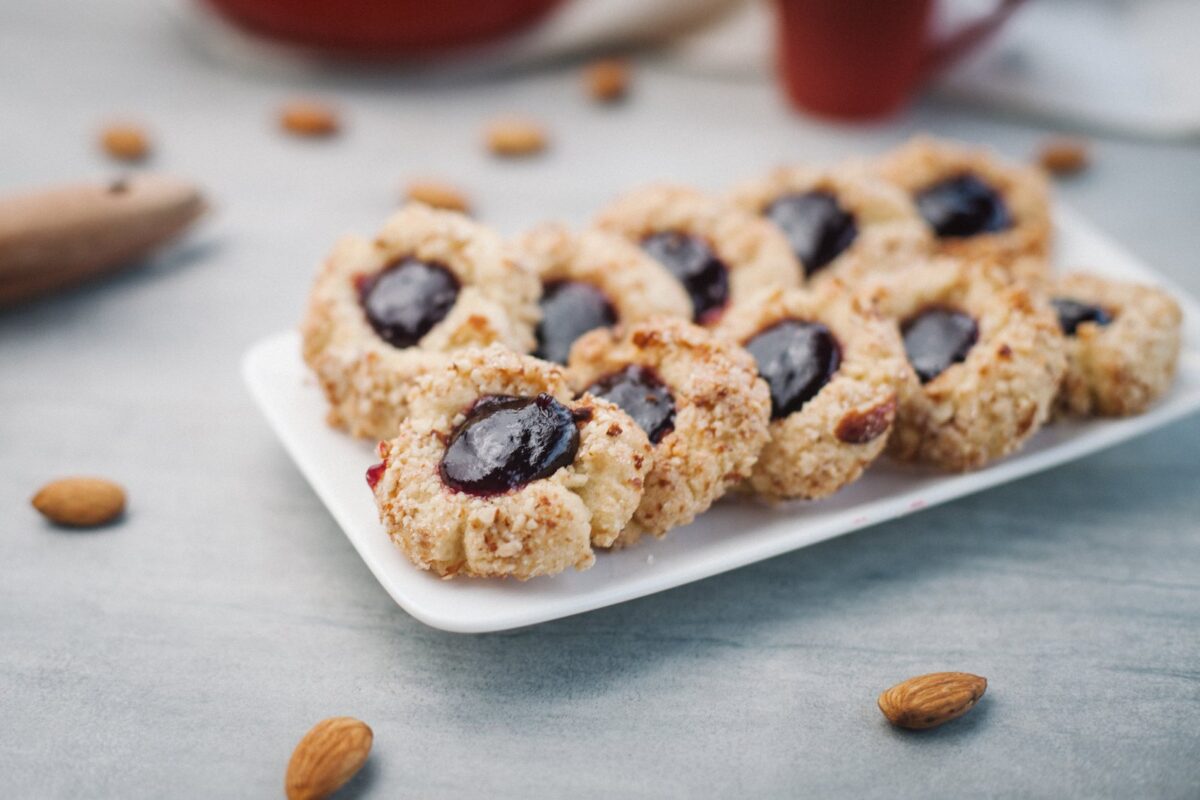 Galletas de mora y almendras sobre una bandeja blanca, con almendras alrededor