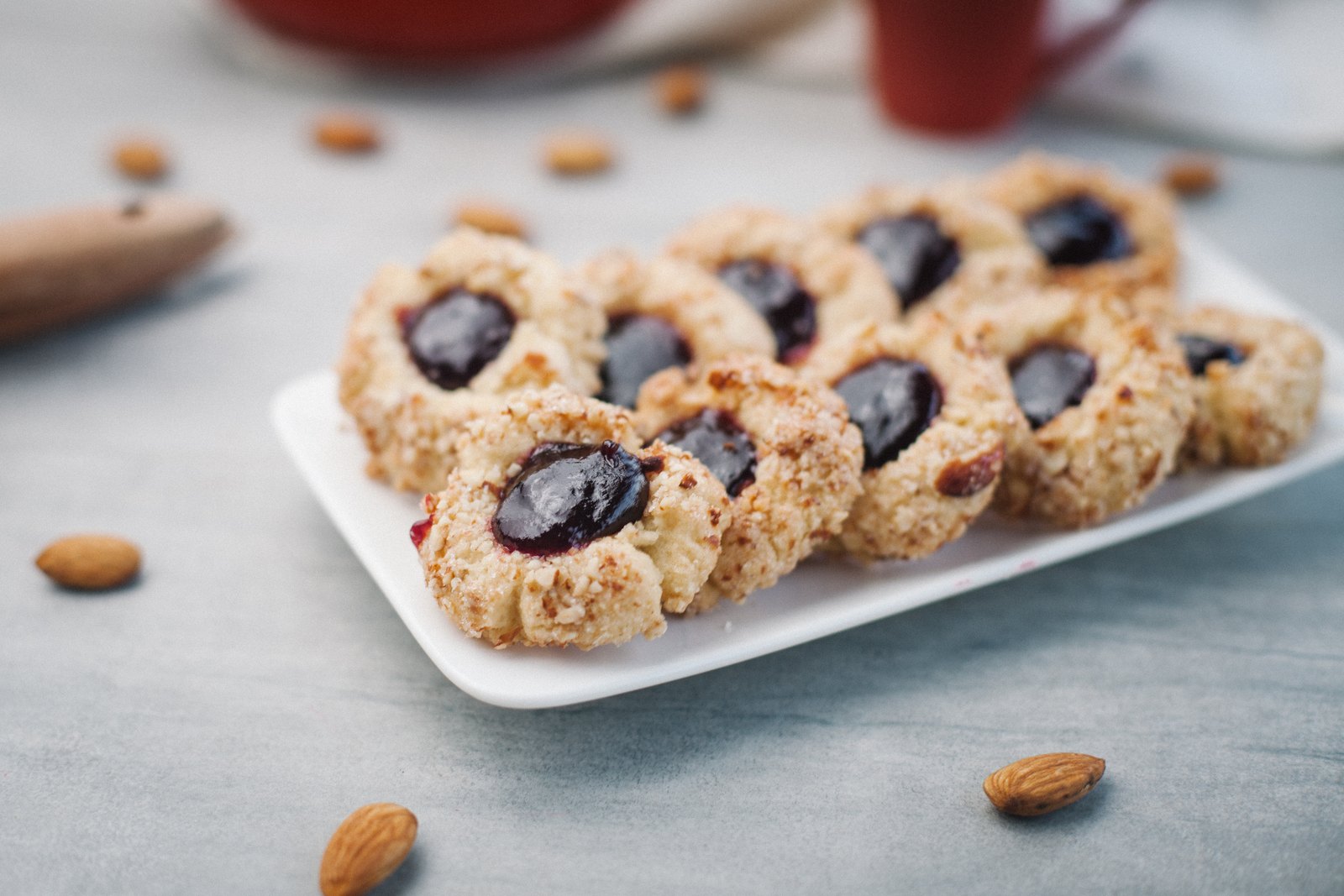 Galletas de mora y almendras sobre una bandeja blanca, con almendras alrededor