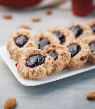 Galletas de mora y almendras sobre una bandeja blanca, con almendras alrededor